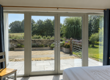 Bright bedroom with large glazed doors demonstrating how solar window film can reduce heat and glare while maintaining natural light and outside views.